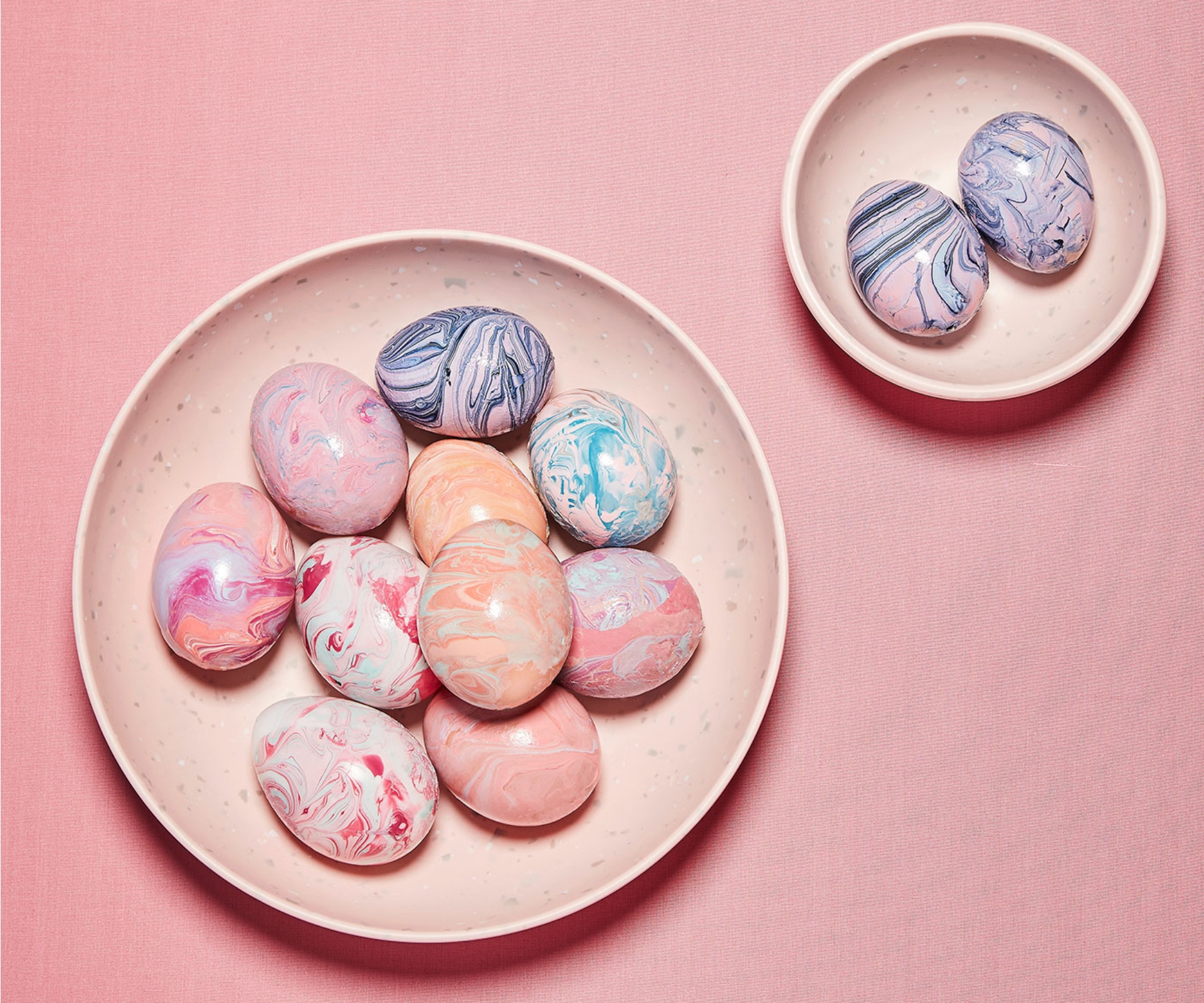 Marbled pastel Easter eggs in two bowls on a pink background.
